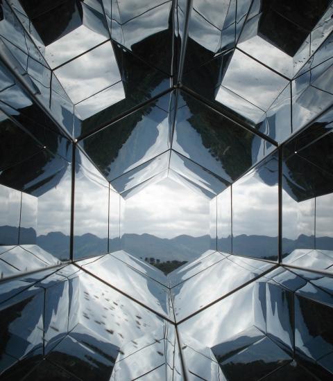 reflective, hexagonal architectural forms looking towards a distant tree-lined horizon